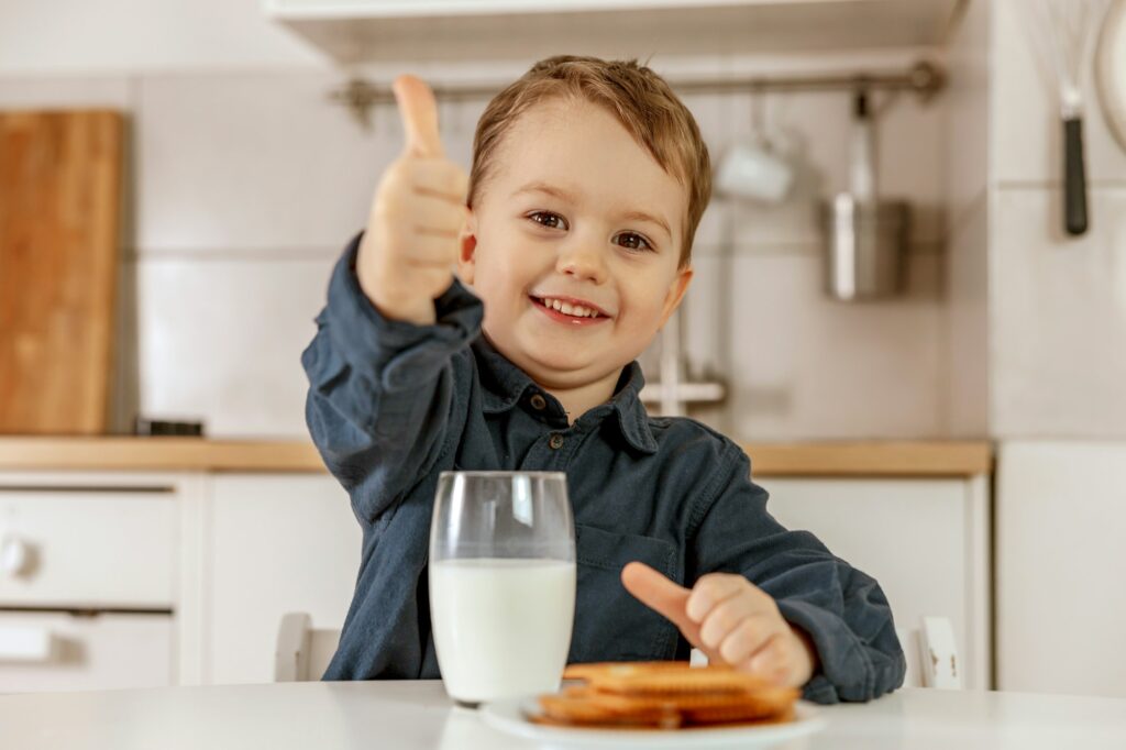 Little boy sitting in the kitchen and drinking milk. Fresh milk in glass, dairy healthy drink.